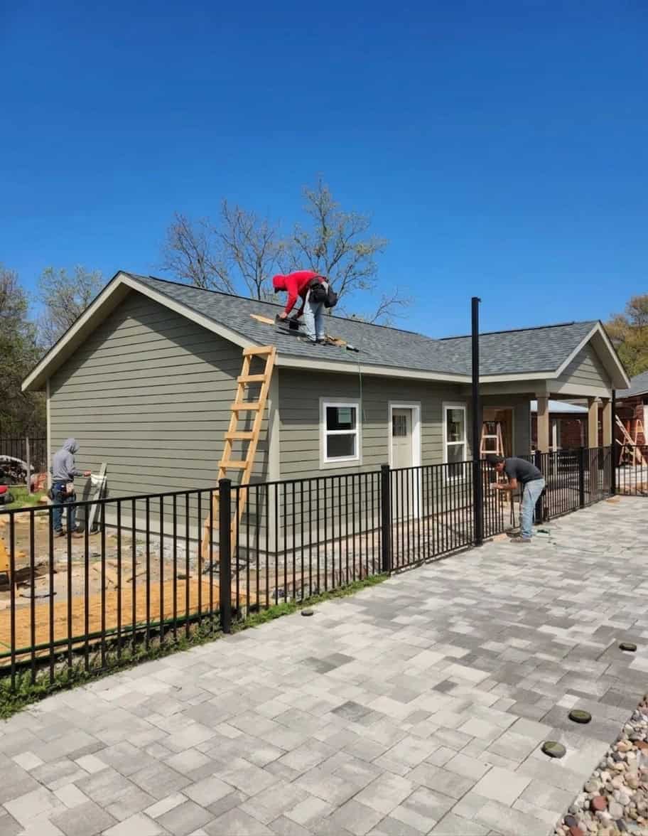Gray-sided residential construction project with workers installing a roof